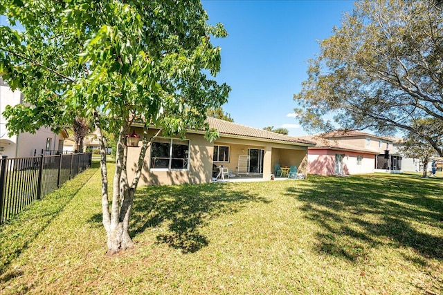 back of house with a tile roof, a yard, fence, and stucco siding