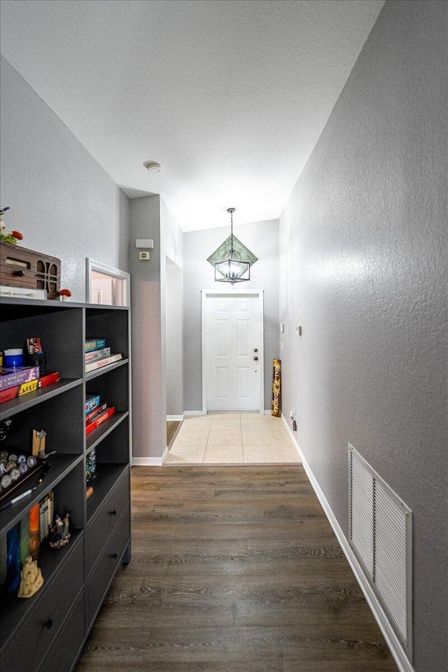 hallway with wood finished floors, visible vents, a textured wall, and baseboards