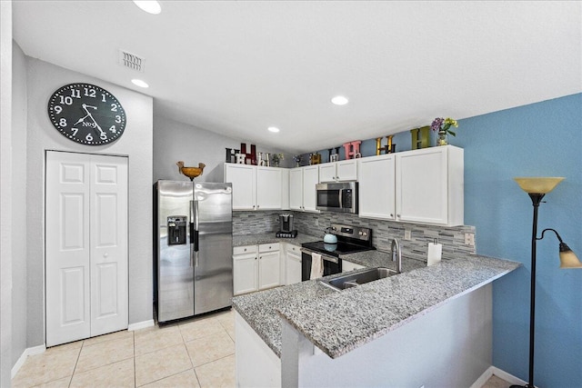 kitchen featuring light tile patterned floors, a peninsula, white cabinets, appliances with stainless steel finishes, and backsplash