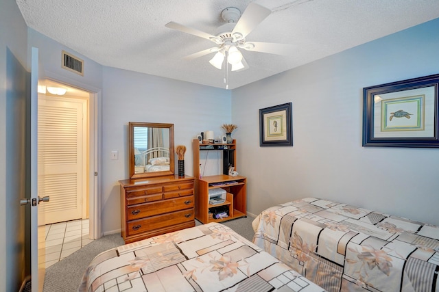 carpeted bedroom featuring tile patterned flooring, visible vents, baseboards, a textured ceiling, and a ceiling fan