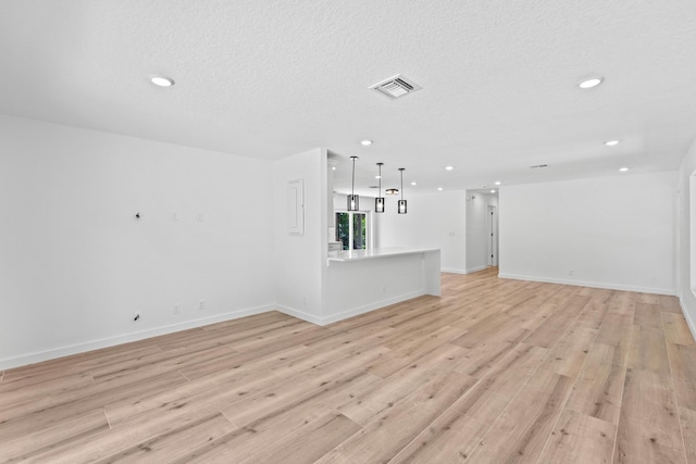 unfurnished living room with recessed lighting, light wood-style flooring, baseboards, and a textured ceiling