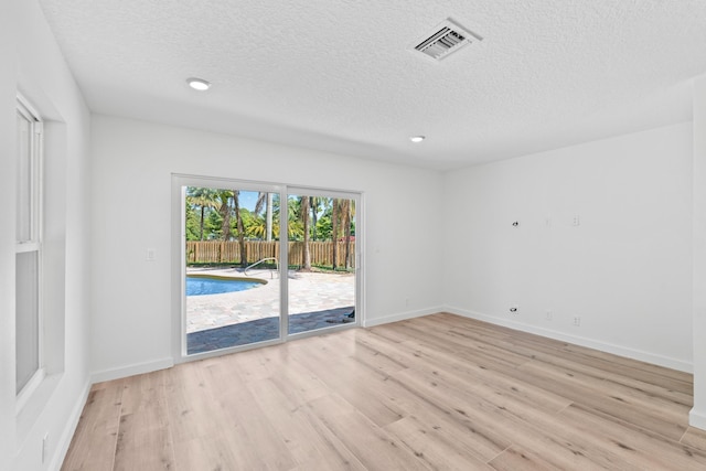 unfurnished room with visible vents, baseboards, light wood-style floors, and a textured ceiling