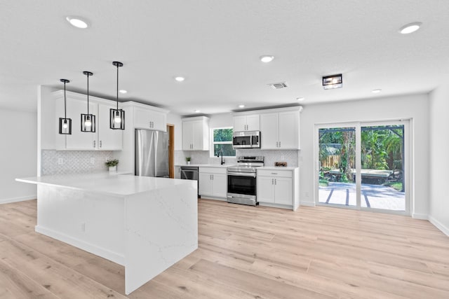 kitchen with light wood finished floors, visible vents, appliances with stainless steel finishes, a peninsula, and white cabinets