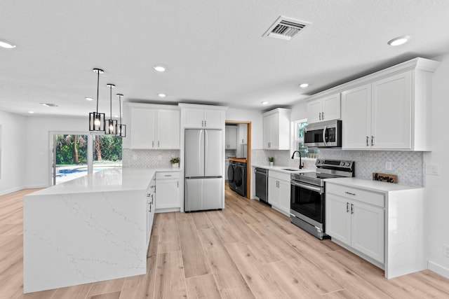 kitchen featuring visible vents, a sink, appliances with stainless steel finishes, a peninsula, and light wood finished floors