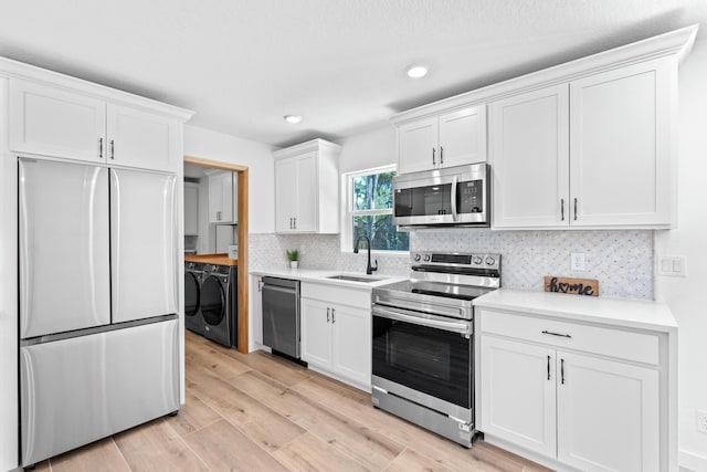 kitchen with independent washer and dryer, a sink, white cabinetry, stainless steel appliances, and light wood-style floors