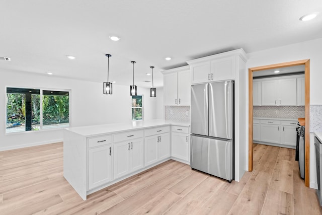 kitchen with light wood-type flooring, light countertops, a peninsula, freestanding refrigerator, and white cabinets