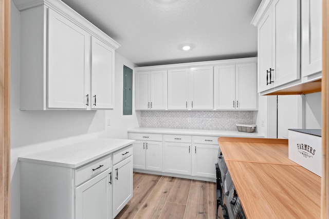 kitchen featuring wooden counters, electric panel, decorative backsplash, light wood-style flooring, and white cabinetry