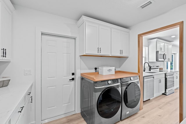 washroom with visible vents, light wood-style flooring, cabinet space, a sink, and washer and dryer