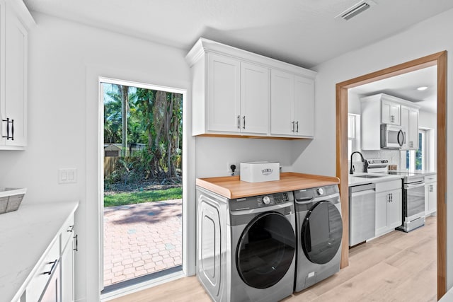 laundry area featuring visible vents, cabinet space, a sink, light wood-style floors, and independent washer and dryer