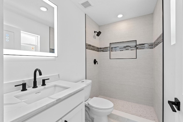 bathroom with a tile shower, toilet, vanity, and recessed lighting