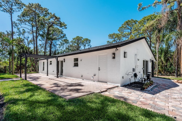 rear view of house featuring a patio area, stucco siding, a pergola, and a yard