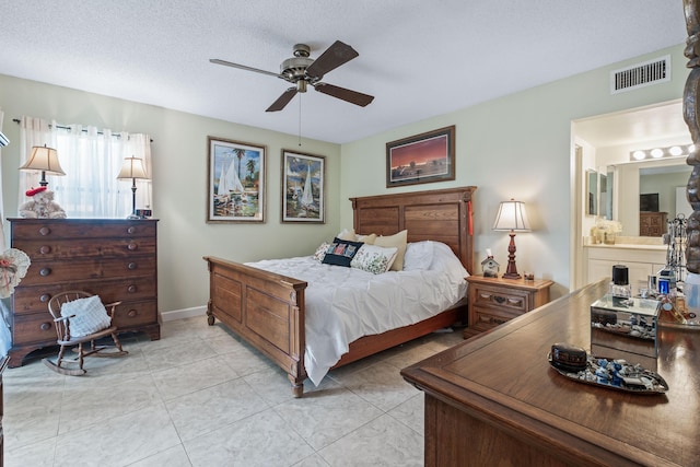 bedroom featuring light tile patterned floors, a ceiling fan, visible vents, ensuite bath, and a textured ceiling