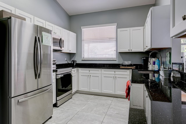 kitchen with a sink, dark stone countertops, white cabinets, and stainless steel appliances