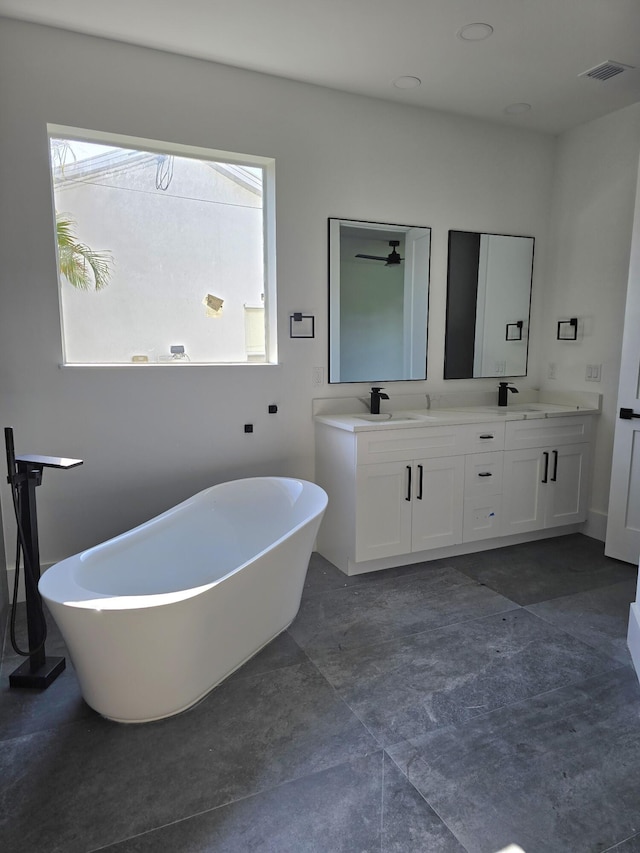 full bathroom with double vanity, a freestanding tub, visible vents, and a sink