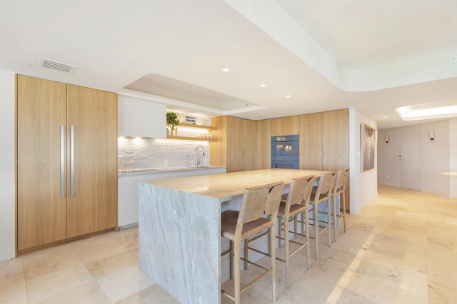 kitchen featuring visible vents, open shelves, a sink, light countertops, and a raised ceiling