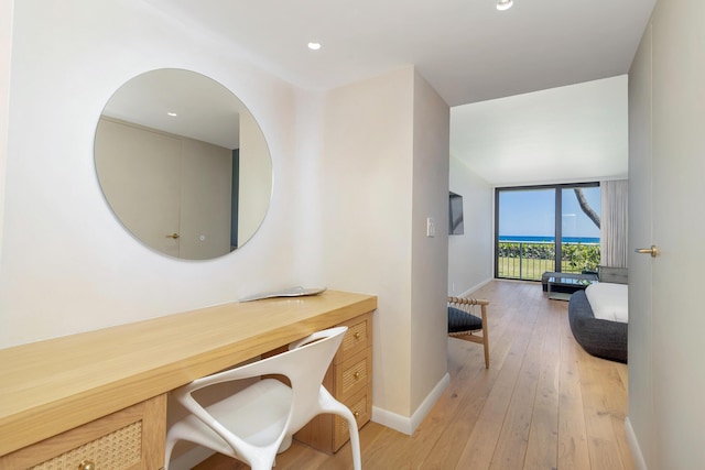 hallway with baseboards, light wood-type flooring, and expansive windows