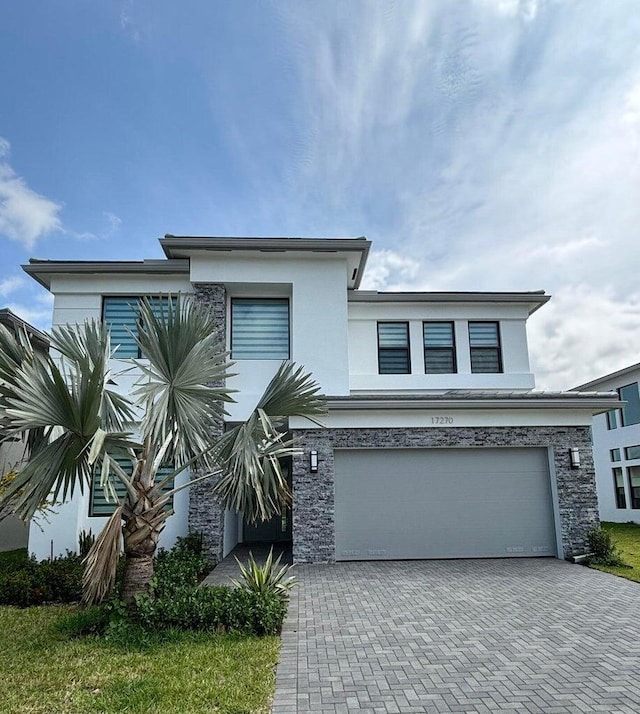 view of front facade with decorative driveway, stone siding, a garage, and stucco siding