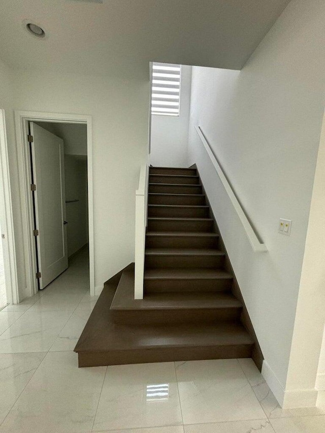 stairway featuring marble finish floor and baseboards