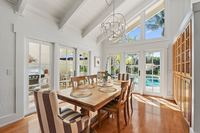 dining area featuring high vaulted ceiling, light wood-style flooring, beamed ceiling, a textured wall, and a chandelier