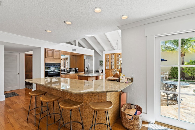 kitchen with dobule oven black, a kitchen island, wood finished floors, stainless steel fridge with ice dispenser, and lofted ceiling