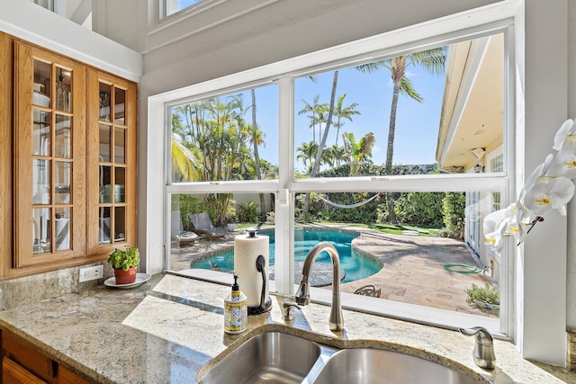 kitchen featuring a sink, glass insert cabinets, light stone countertops, and brown cabinetry