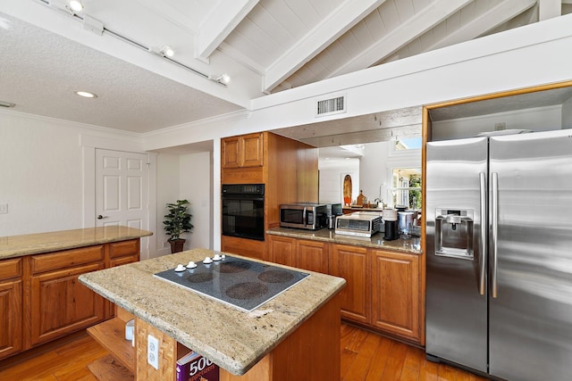 kitchen with visible vents, a kitchen island, vaulted ceiling with beams, brown cabinets, and black appliances