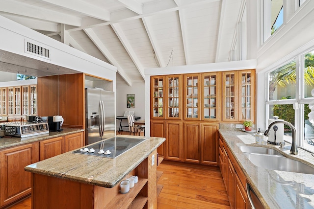 kitchen featuring visible vents, a sink, stainless steel fridge, brown cabinetry, and black electric stovetop