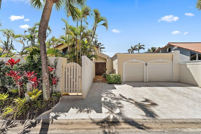 view of front of property with stucco siding, a gate, decorative driveway, fence, and an attached garage