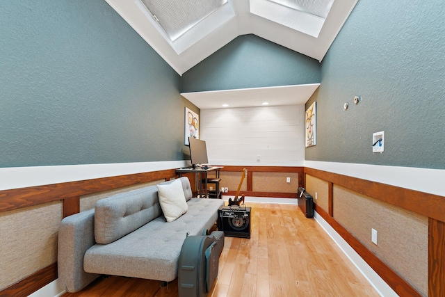 living area with vaulted ceiling with skylight, wood finished floors, wainscoting, and a textured wall