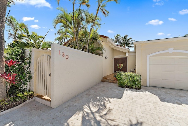 view of property exterior with stucco siding, a gate, decorative driveway, fence, and an attached garage