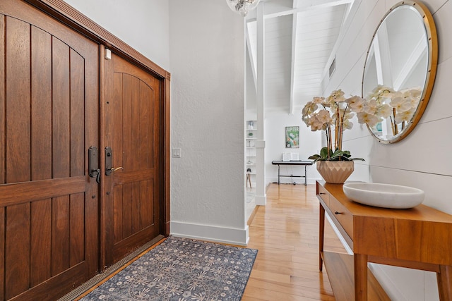 entryway with beamed ceiling, baseboards, visible vents, and light wood-style flooring