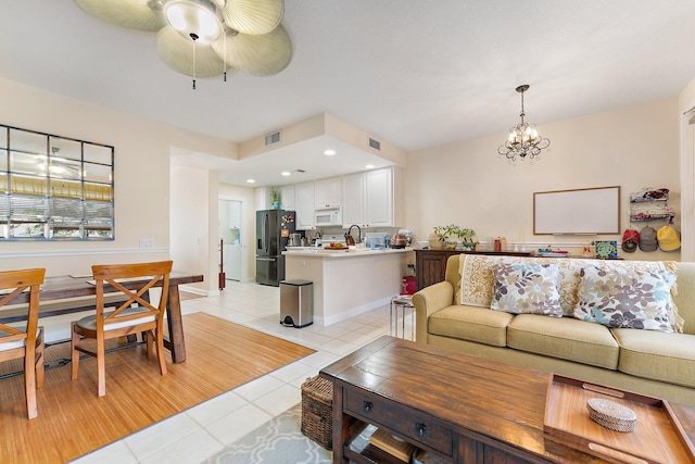 living room featuring light tile patterned floors, visible vents, ceiling fan with notable chandelier, and baseboards