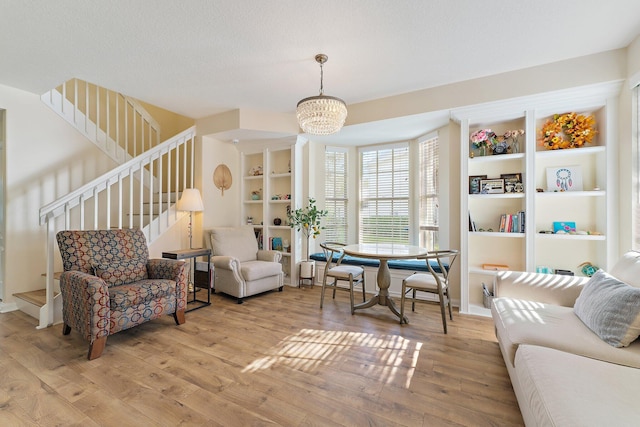 living room with built in features, an inviting chandelier, stairs, a textured ceiling, and light wood-type flooring