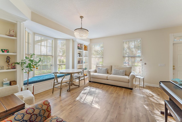 living area featuring built in shelves, baseboards, a chandelier, light wood-type flooring, and a textured ceiling