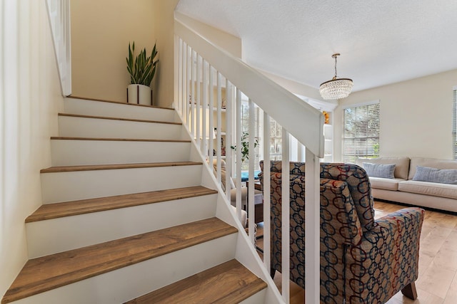 stairway with an inviting chandelier, wood finished floors, and a textured ceiling