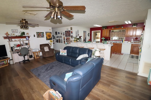 living area with light wood-type flooring, visible vents, a textured ceiling, and ceiling fan