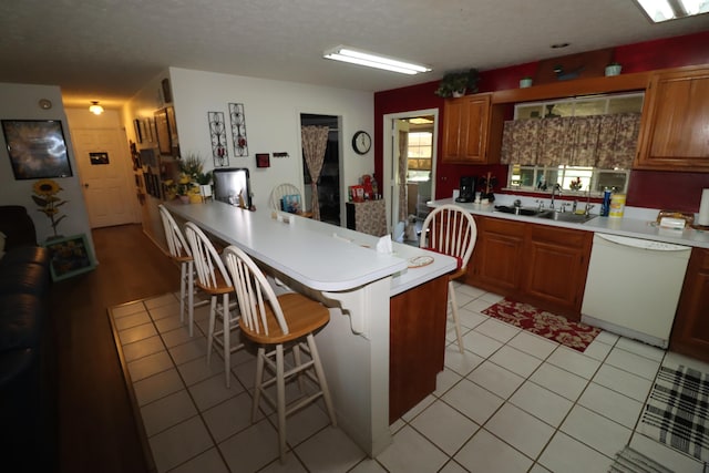 kitchen with light countertops, a kitchen breakfast bar, a peninsula, white dishwasher, and a sink