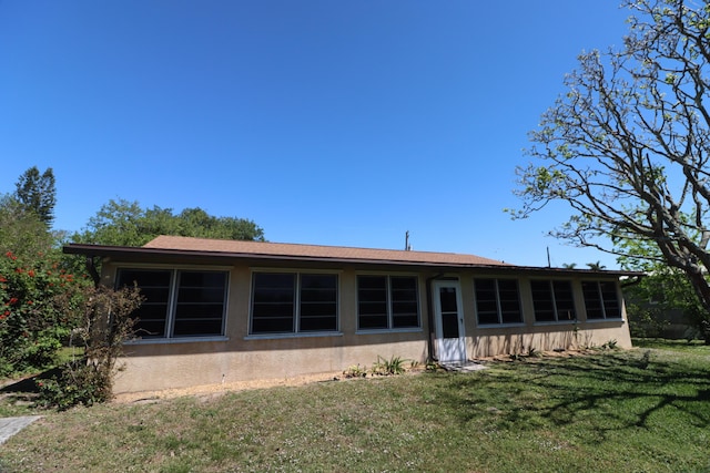 rear view of house with a lawn and stucco siding