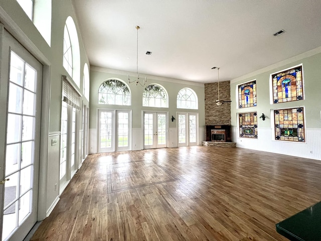 unfurnished living room featuring visible vents, hardwood / wood-style flooring, a fireplace, wainscoting, and a towering ceiling