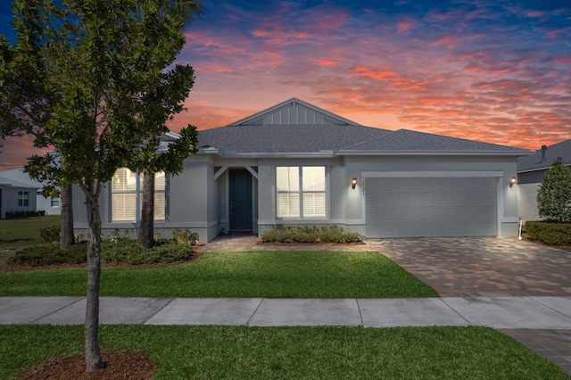 ranch-style house with stucco siding, decorative driveway, a yard, roof with shingles, and an attached garage