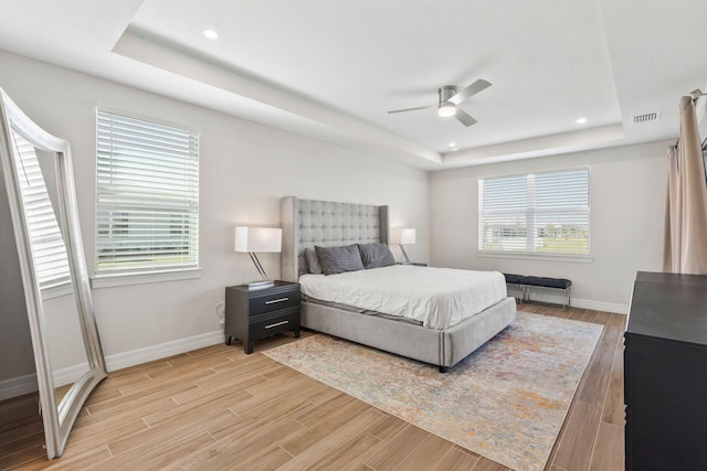 bedroom featuring visible vents, a raised ceiling, multiple windows, and light wood finished floors