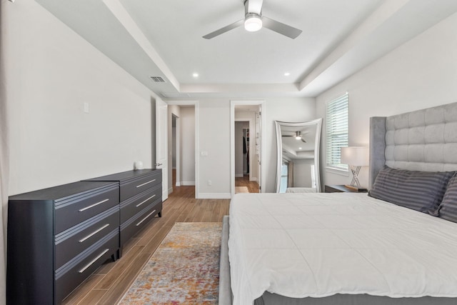 bedroom featuring visible vents, baseboards, wood finish floors, a tray ceiling, and recessed lighting