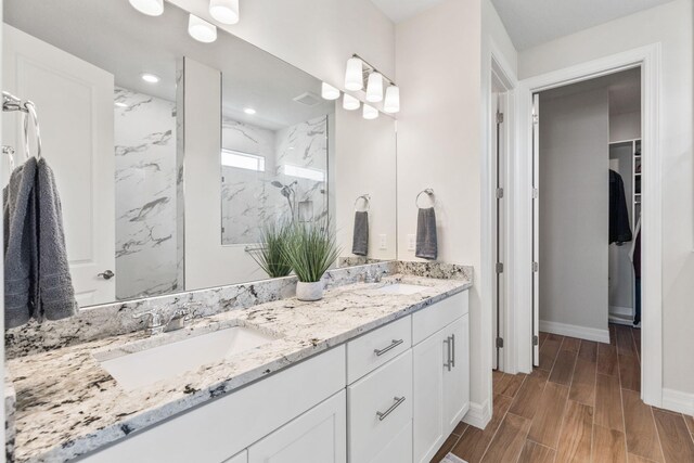 full bath with double vanity, wood finish floors, a marble finish shower, and a sink