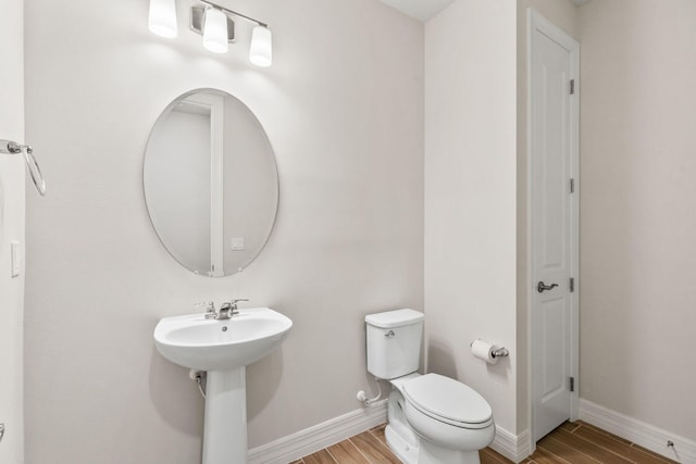 bathroom featuring a sink, toilet, baseboards, and wood tiled floor