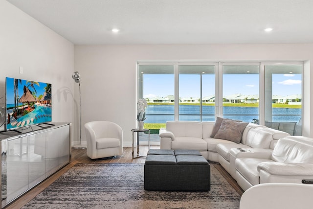 living area with recessed lighting, plenty of natural light, wood finished floors, and a water view