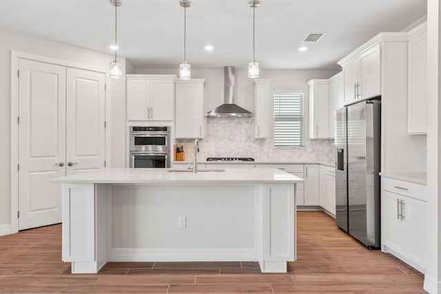 kitchen with light wood-style flooring, appliances with stainless steel finishes, wall chimney exhaust hood, and a sink