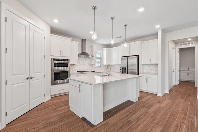 kitchen with visible vents, white cabinets, stainless steel appliances, wall chimney exhaust hood, and a sink