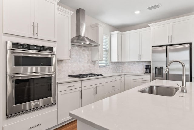 kitchen with a sink, appliances with stainless steel finishes, light countertops, and wall chimney range hood