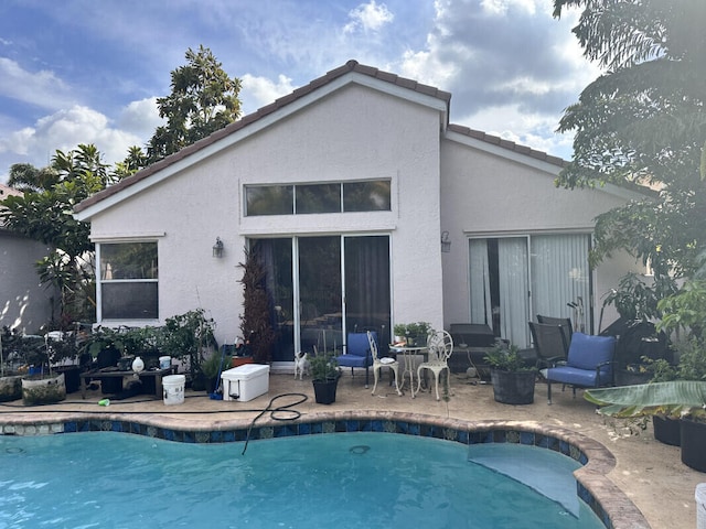 rear view of property with stucco siding, an outdoor pool, and a patio