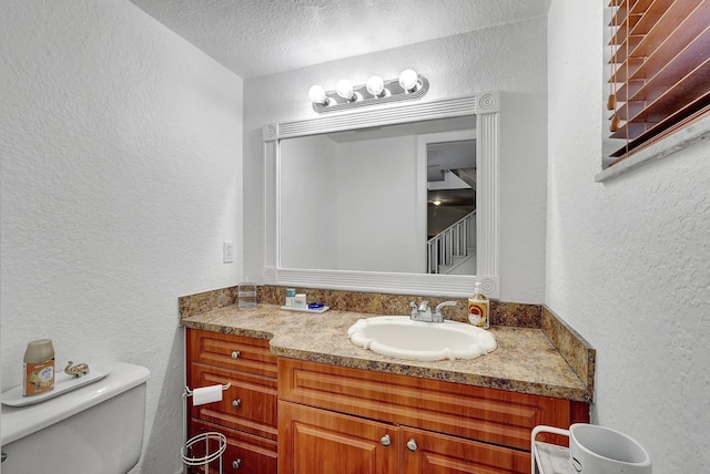 bathroom with a textured ceiling, toilet, vanity, and a textured wall